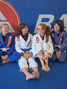 Home 14 Woman in a Brazilian Jiu-Jitsu gi standing confidently on the mats at a martial arts academy.